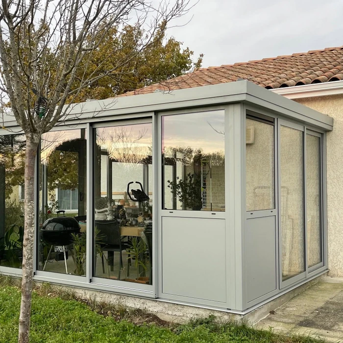 Façade extérieure d'une maison avec une fenêtre coulissante aluminium anthracite à trois vantaux, encadrée d'un dormant en pierre reconstituée blanche