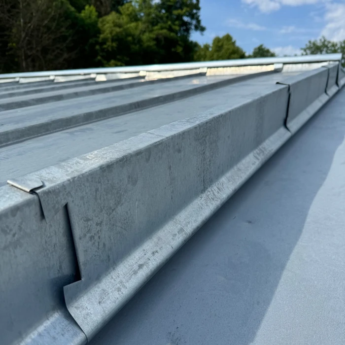 Toiture métallique en zinc à joints debout vue en perspective, avec ventilateurs de désenfumage circulaires et une grille de ventilation rectangulaire