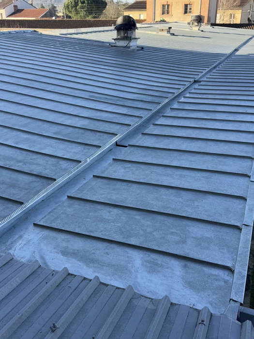 Un technicien en tenue bleue installe ou répare une gouttière sur une maison résidentielle