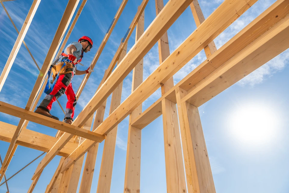 Un travailleur de la construction se concentre sur l'installation de poutres en bois dans un espace mansardé pendant la rénovation d'une maison