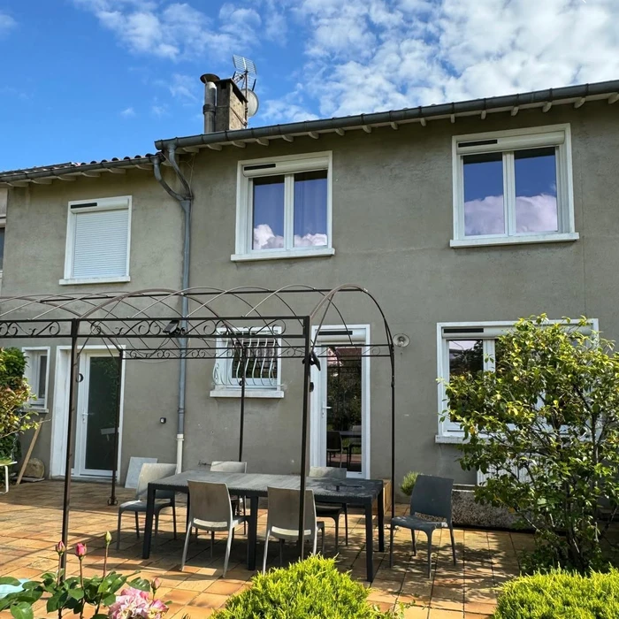 Terrasse en bois résineux massif neuf, couverte par une charpente en chêne à entraits et poteaux apparents, rattachée à une bâtisse en pierre calcaire avec toiture en tuiles canal