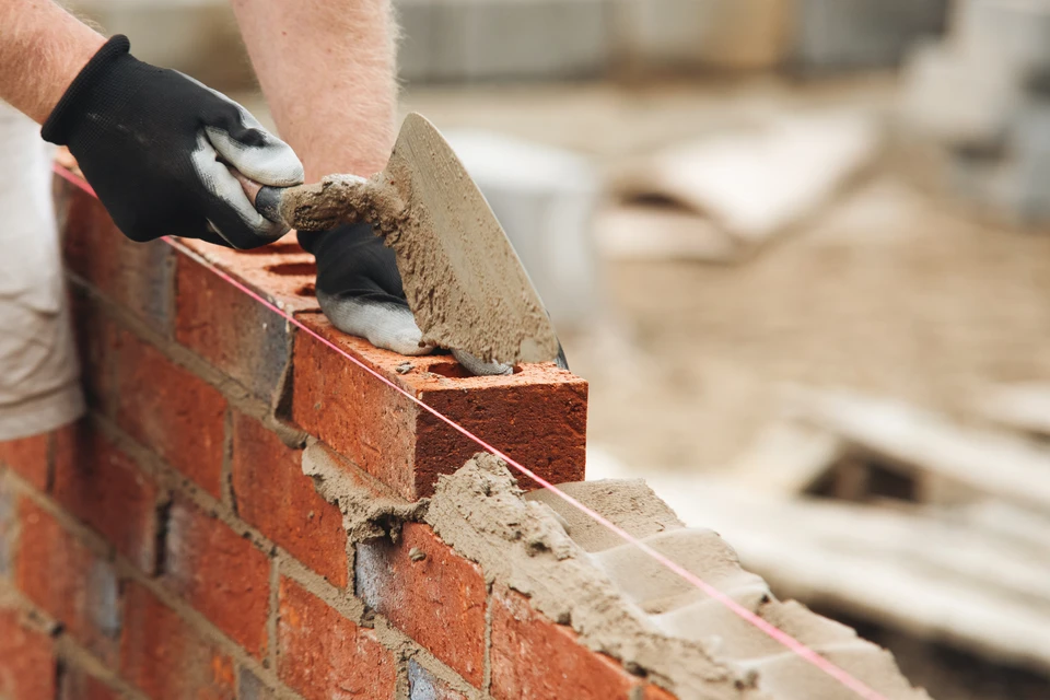 Chantier de construction extérieur avec ouvrier en combinaison et gants orange travaillant sur fondations