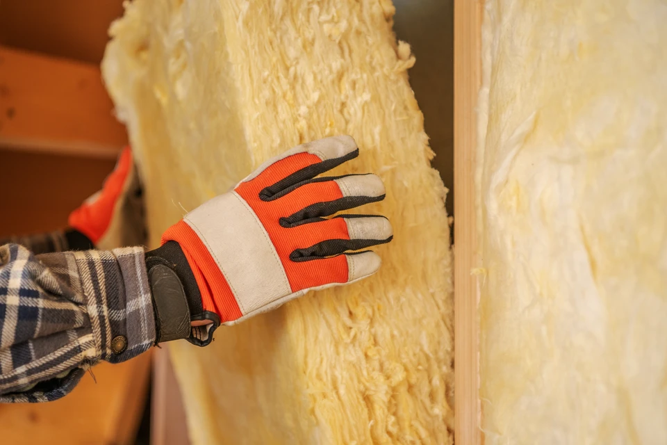Ouvrier maçon construisant un mur en briques rouges sur chantier extérieur, portant gants de protection jaunes et chemise à carreaux