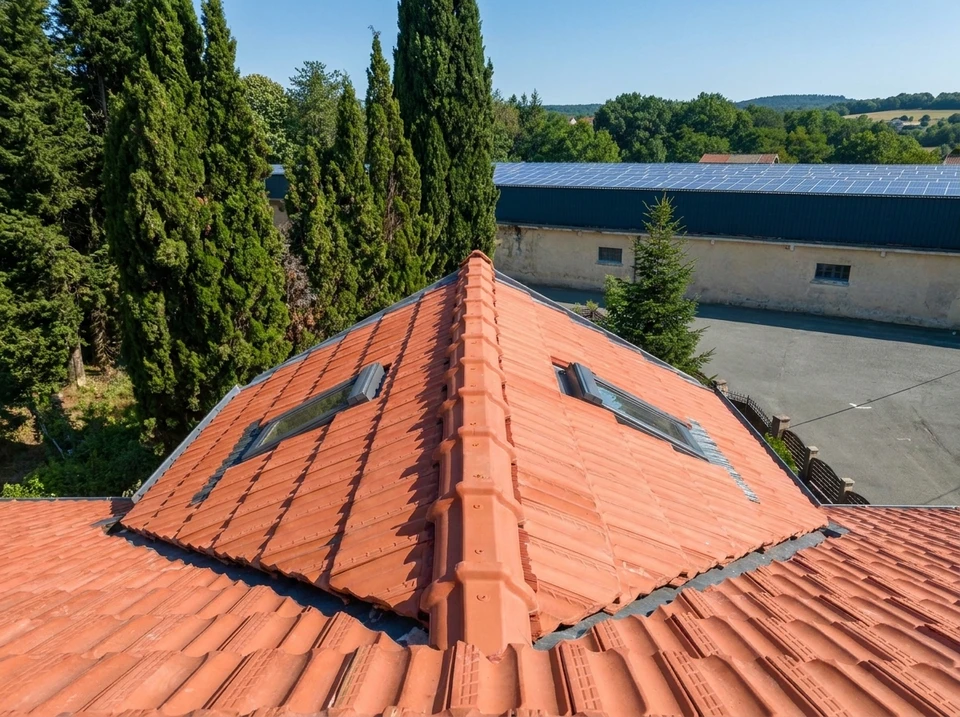 Extérieur d'une maison avec cheminée en briques rouges et oranges détériorées, toit à versant rouge écaillé, ciel bleu nuageux