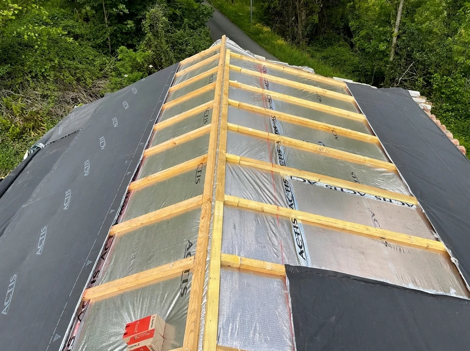 Chantier de construction résidentielle en cours, combles aménageables avec charpente bois apparente et isolation thermique jaune entre chevrons
